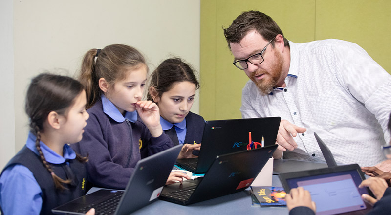 Students with their teacher learning around a laptop at St Michael's Primary School Blacktown South