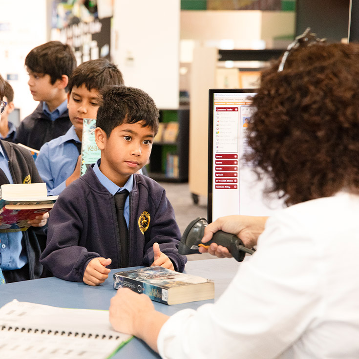 Student checking out books from the school library at St Michael's Primary School Blacktown South